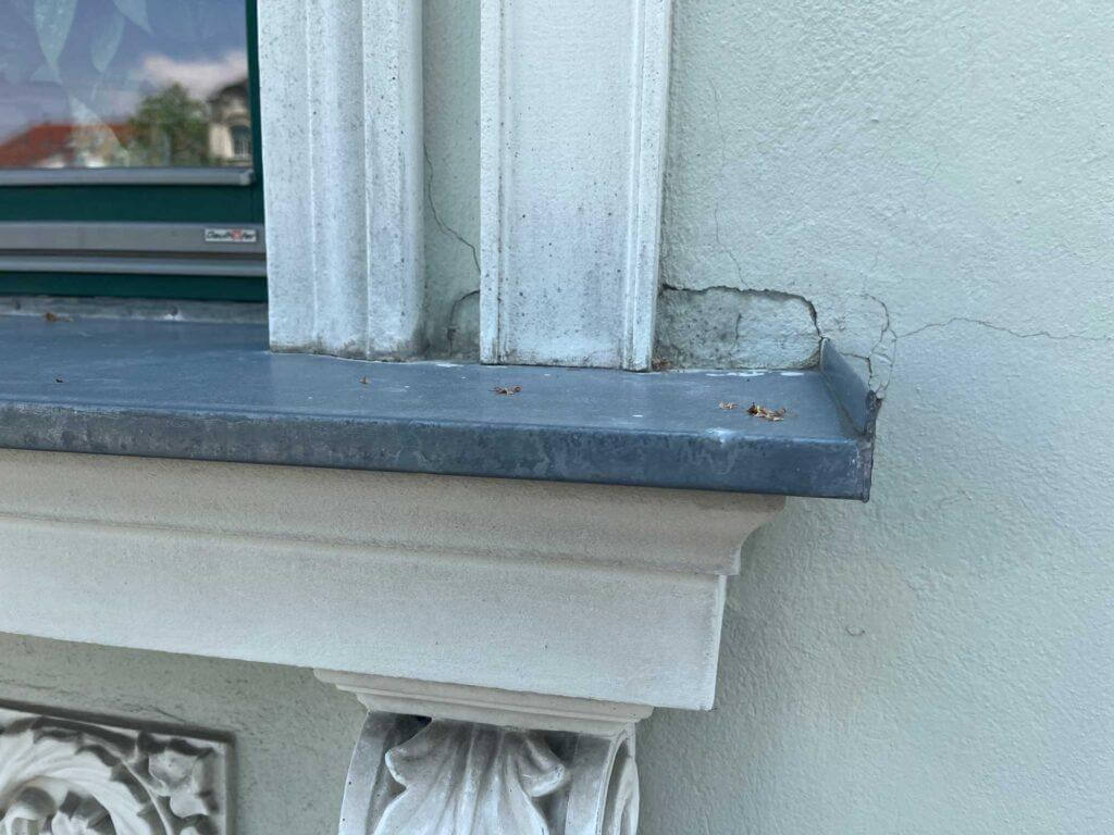 Ausgebrochener Fassadenputz mit Rissbildungen im Bereich der Fensterbankenden